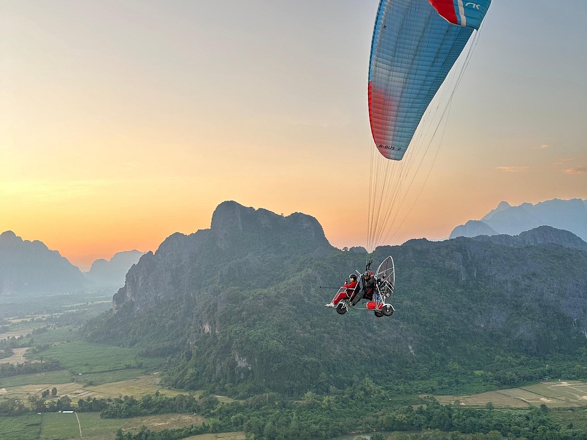A tandem paramotor flying over green mountains at sunset
